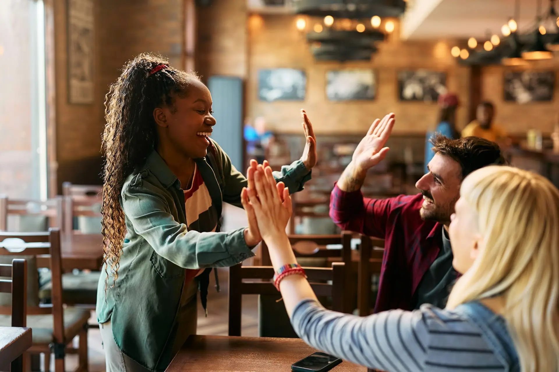 Group of happy friends giving high-five while gathering in a pub.