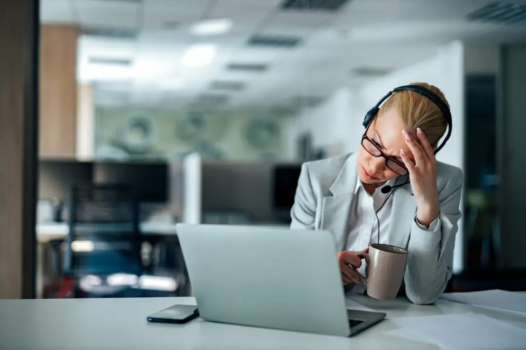 Problems at work. Portrait of a stressed woman with headset and laptop at workplace.