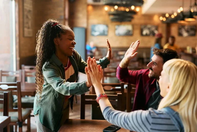 Group of happy friends giving high-five while gathering in a pub.